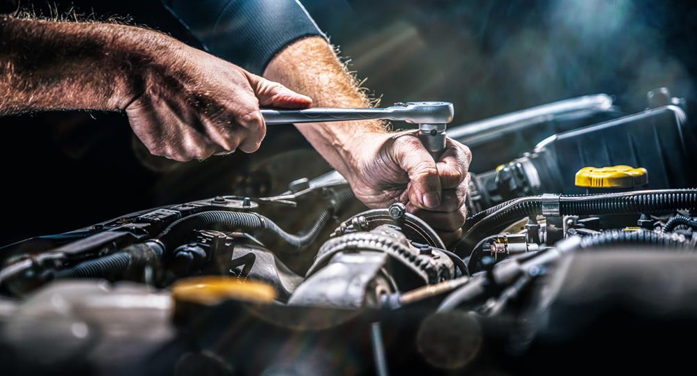 A person uses a wrench to install a transmission in a car