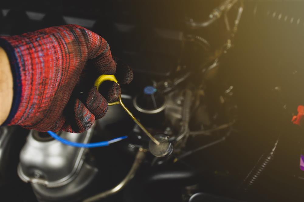 A person wearing a red glove pulls out the transmission dipstick