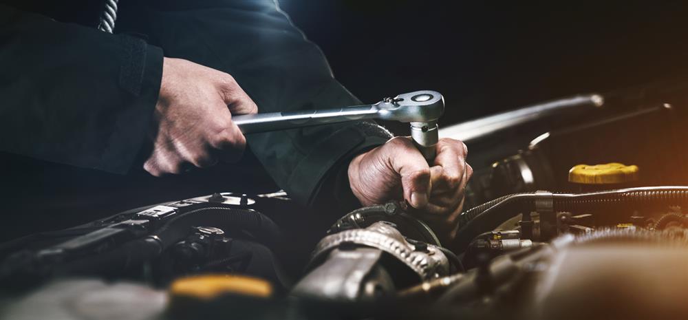 A mechanic uses a wrench to work on a car engine.